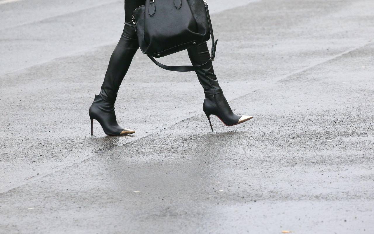 Frau mit High Heels geht über eine regennasse Straße