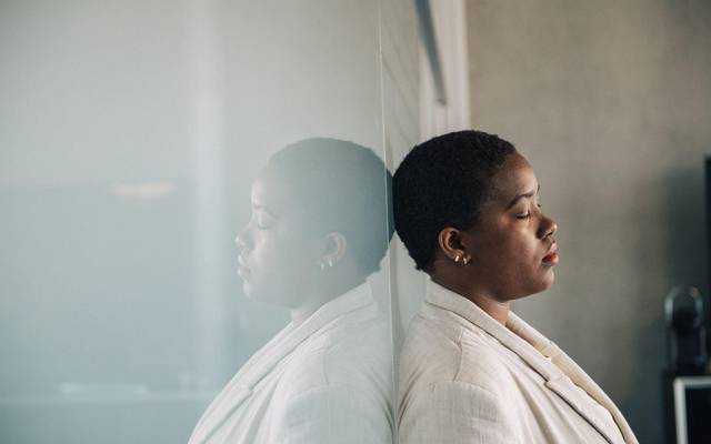 Eine junge Frau lehnt nachdenklich an einer Glaswand