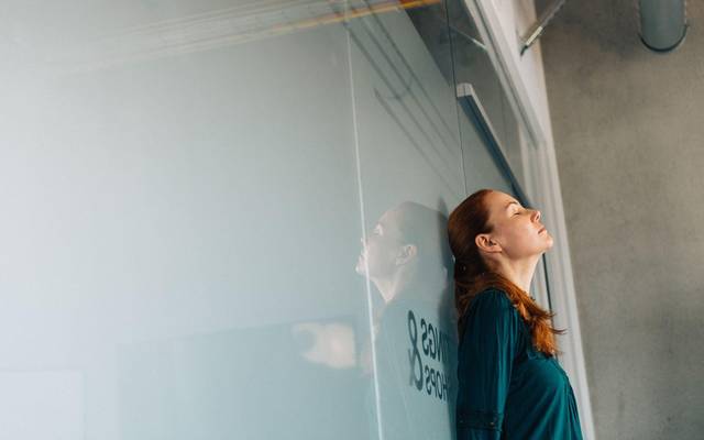 Eine Frau lehnt erschöpft an einer Glaswand im Büro