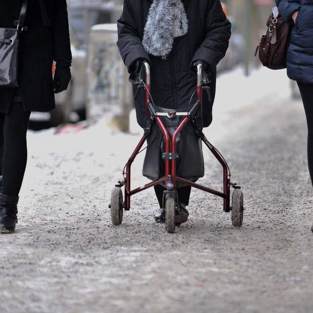 Ein Frau geht mit Rollator auf einem schneebedeckten Gehweg