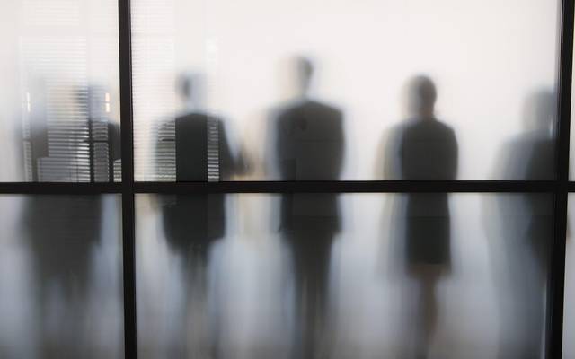 Personen stehen hinter eine Glasscheibe in einem Büro