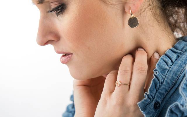 Frau fasst sich an den Hals