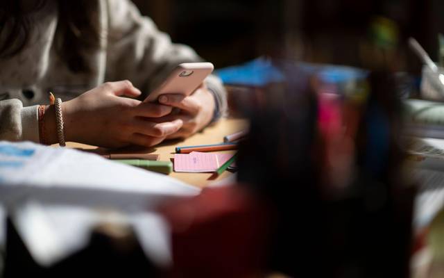 Eine Jugendliche sitzt mit Smartphone an einem Schreibtisch