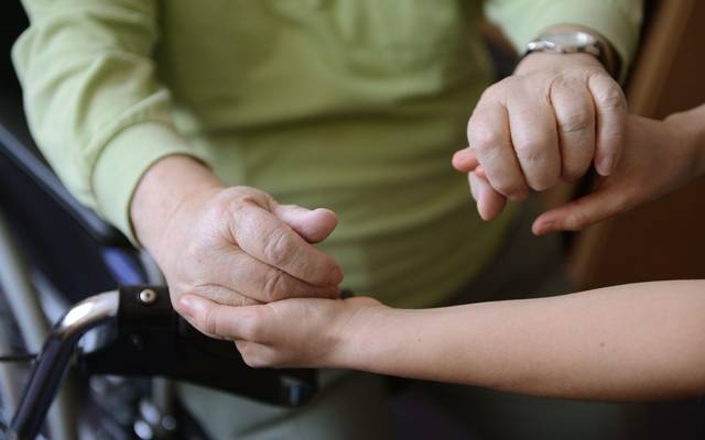 Eine junge Frau hält die Hände eines alten Mannes